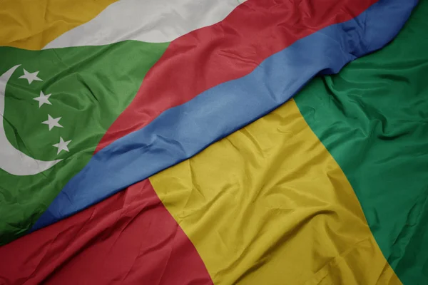 Waving colorful flag of guinea and national flag of comoros. — Stock Photo, Image
