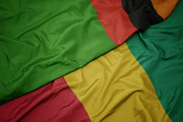 Schwenken bunte Flagge von Guinea und Nationalflagge von Sambia. — Stockfoto