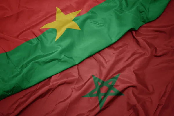 Schwenken bunte Flagge Marokkos und Nationalflagge der Burkina Faso. — Stockfoto