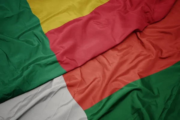 Ondeando colorida bandera de madagascar y bandera nacional de benin . — Foto de Stock