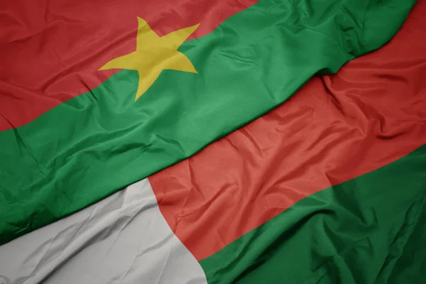 Ondeando colorida bandera de madagascar y bandera nacional de burkina faso . —  Fotos de Stock