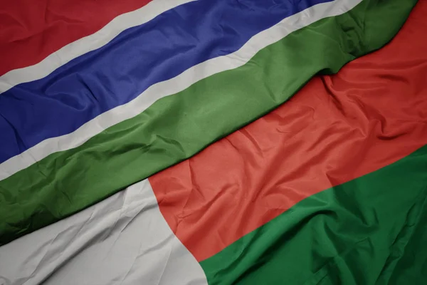 Waving colorful flag of madagascar and national flag of gambia. — Stock Photo, Image
