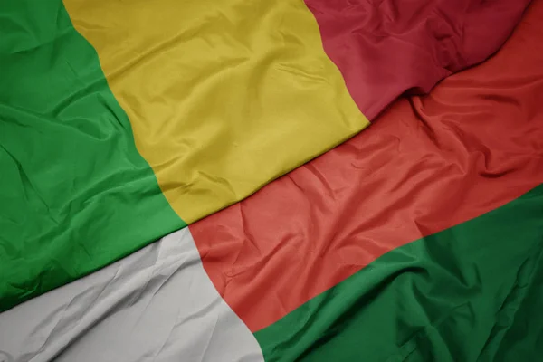 Ondeando colorida bandera de madagascar y bandera nacional de mali . — Foto de Stock