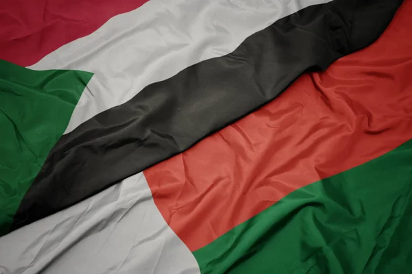 Waving colorful flag of madagascar and national flag of sudan. — Stock Photo, Image