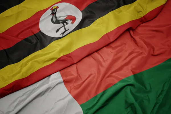 Waving colorful flag of madagascar and national flag of uganda. — Stock Photo, Image