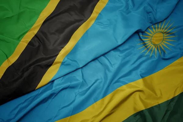 waving colorful flag of rwanda and national flag of tanzania.