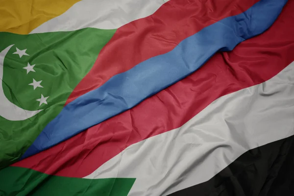 Ondeando colorida bandera de sudan y bandera nacional de comoras . — Foto de Stock
