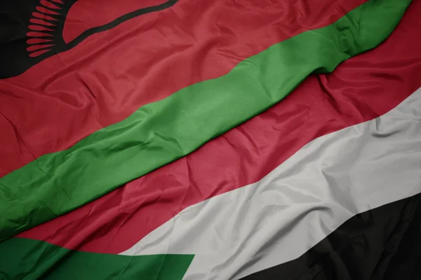 Agitant drapeau coloré de soudan et drapeau national de malawi . — Photo