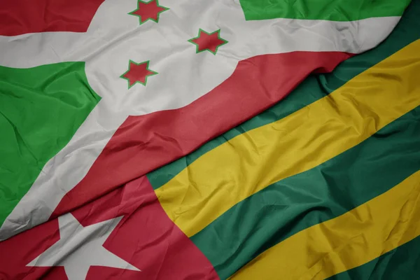 Schwenken bunte Flagge von Togo und Nationalflagge von Burundi . — Stockfoto
