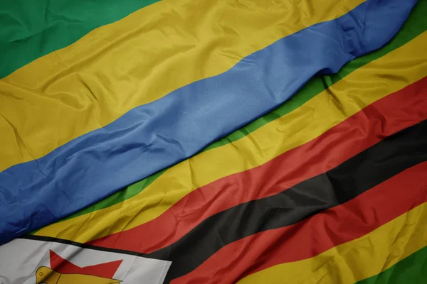 Stock image waving colorful flag of zimbabwe and national flag of gabon.