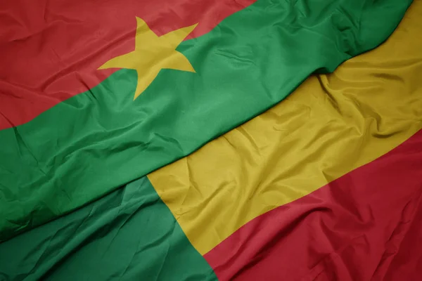 Ondeando colorida bandera de benin y bandera nacional de burkina faso . — Foto de Stock