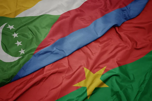 Ondeando colorida bandera de Burkina faso y bandera nacional de comoras . — Foto de Stock