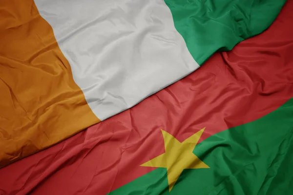 Ondeando colorida bandera de Burkina faso y bandera nacional de cote divoire . —  Fotos de Stock