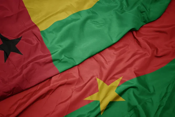 Ondeando colorida bandera de burkina faso y bandera nacional de guinea bissau . — Foto de Stock