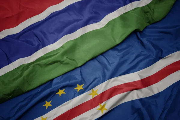 Mávání barevnou vlajkou Cape Verde a národní vlajka gamia. — Stock fotografie