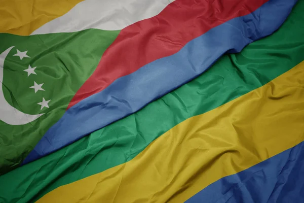 Ondeando colorida bandera de gabón y bandera nacional de comoras . — Foto de Stock