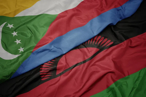 Ondeando colorida bandera de Malawi y bandera nacional de Comoras . — Foto de Stock