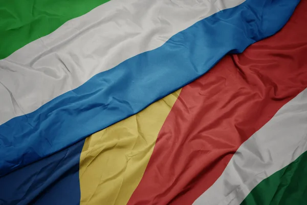 Schwenken bunte Flagge der seychellen und Nationalflagge von Sierra Leone. — Stockfoto