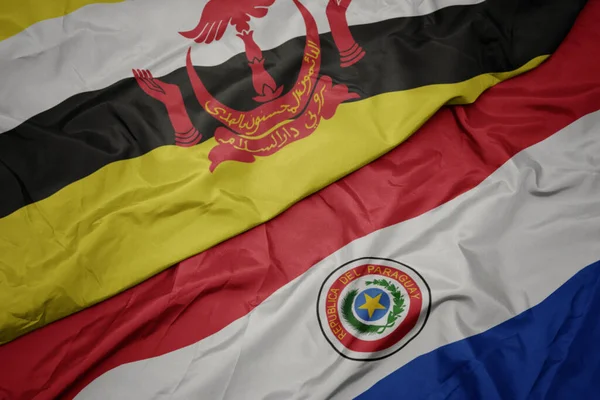 waving colorful flag of paraguay and national flag of brunei. macro