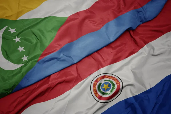 waving colorful flag of paraguay and national flag of comoros. macro