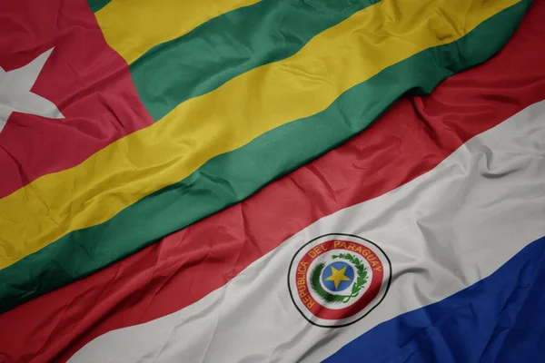 waving colorful flag of paraguay and national flag of togo. macro