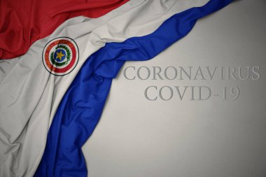 waving colorful national flag of paraguay on a gray background with text coronavirus covid-19 . concept. clipart