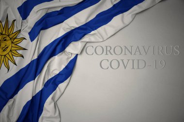 Koronavirüs covid-19 yazılı gri bir arka planda renkli Uruguay bayrağı sallıyordu. konsept.
