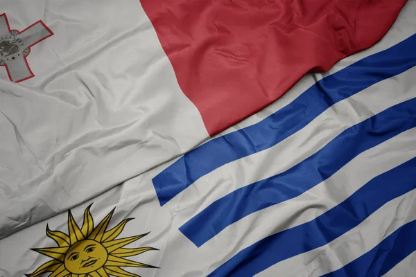 waving colorful flag of uruguay and national flag of malta. macro