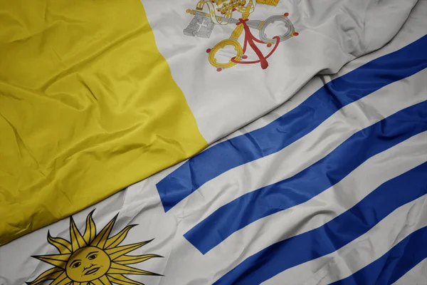 waving colorful flag of uruguay and national flag of vatican city. macro