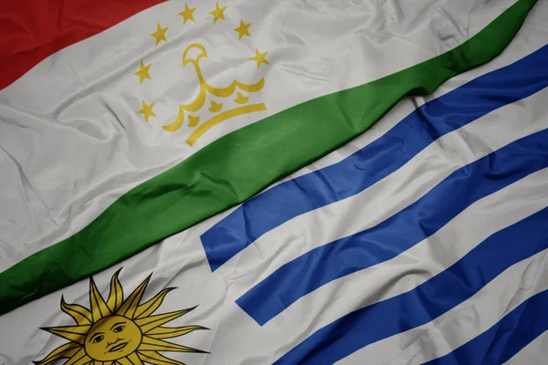 waving colorful flag of uruguay and national flag of tajikistan. macro