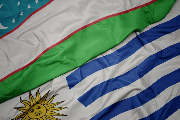 waving colorful flag of uruguay and national flag of uzbekistan. macro