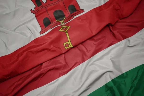 waving colorful flag of hungary and national flag of gibraltar. macro