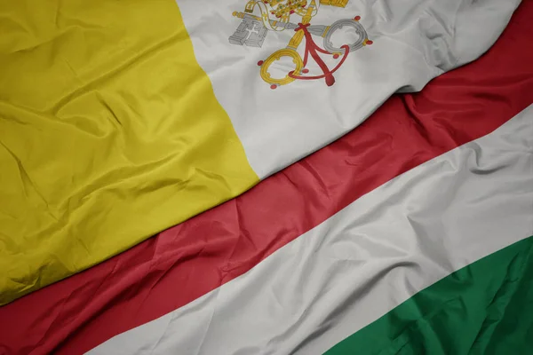 waving colorful flag of hungary and national flag of vatican city. macro