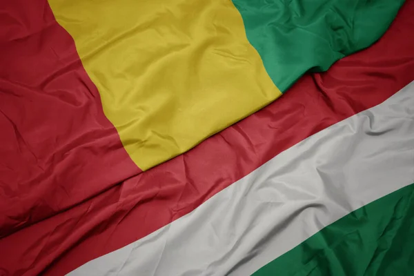 waving colorful flag of hungary and national flag of guinea. macro