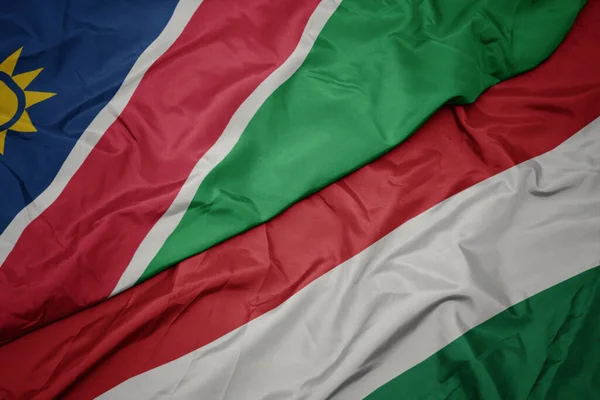 waving colorful flag of hungary and national flag of namibia. macro