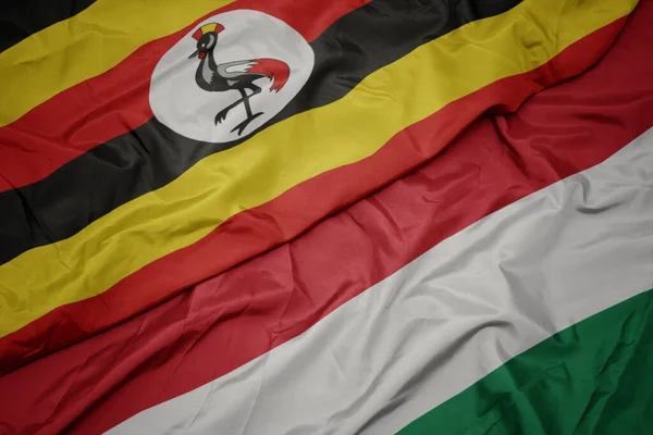 waving colorful flag of hungary and national flag of uganda. macro