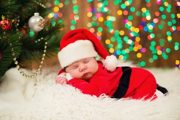 Portrait de nouveau-né en vêtements de Père Noël couché sous l'arbre de Noël . — Photo