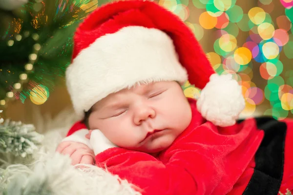 Portret van de pasgeboren baby in Santa kleren liggen onder kerstboom. — Stockfoto