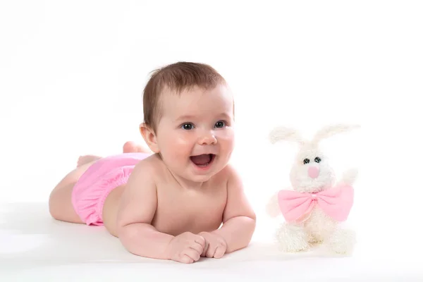 Little girl smiling with a toy rabbit lies on white background. — Stock Photo, Image