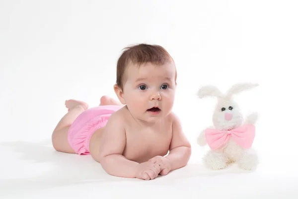 Маленькая девочка улыбается с игрушечным кроликом лежит на белом фоне . — стоковое фото