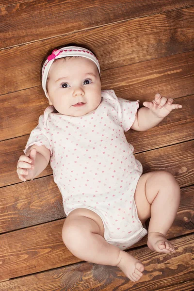 Widok z góry z adorable córeczka ogląda aparat leżąc na podłoże drewniane — Zdjęcie stockowe