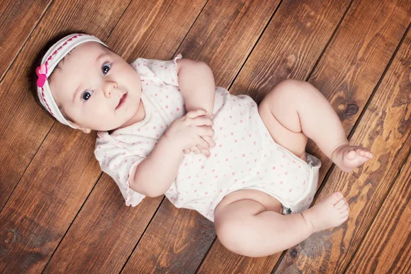 Vista superior de la adorable niña mirando a la cámara mientras está acostada sobre un fondo de madera —  Fotos de Stock