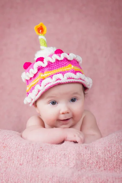 Newborn baby in warm knitted hat the form of cake with a candle — Stock Photo, Image