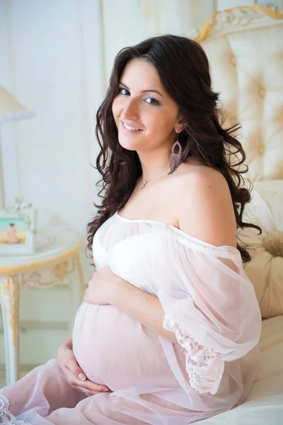 Beautiful pregnant girl in a lace negligee sitting on a bed — Stock Photo, Image