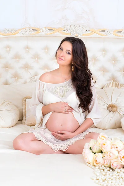 Vacker gravid brunett sitter på en säng i lotusställning — Stockfoto