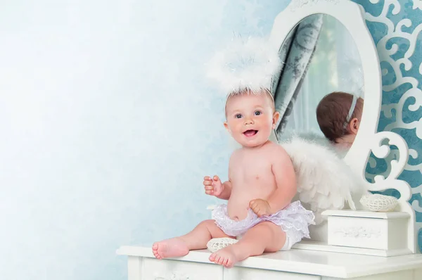 Маленький ангел улыбается и сидит на туалетном столике — стоковое фото