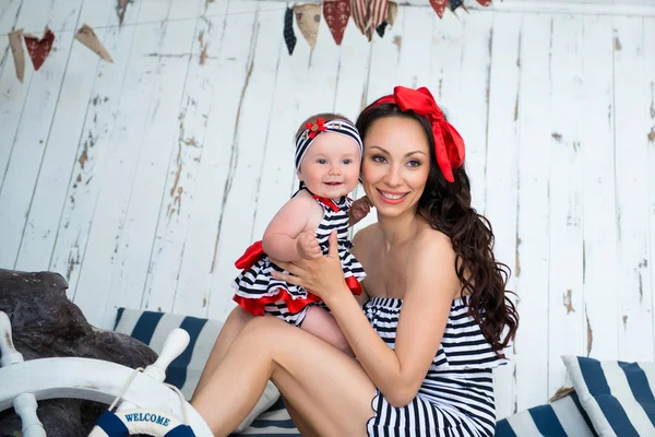 Girl smiling in the arms of my mother in a marine style sitting on the sand. — Stock Photo, Image