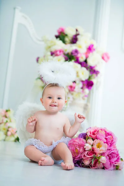 Маленький ангел улыбается и счастлив сидя на фоне цветов и арфы — стоковое фото