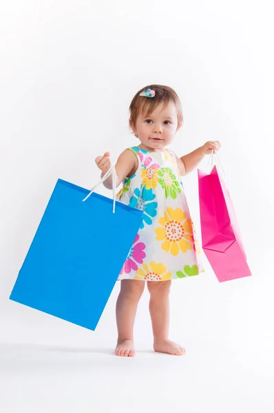 Маленькая девочка, стоящая с цветными бумажными пакетами на белом фоне . — стоковое фото
