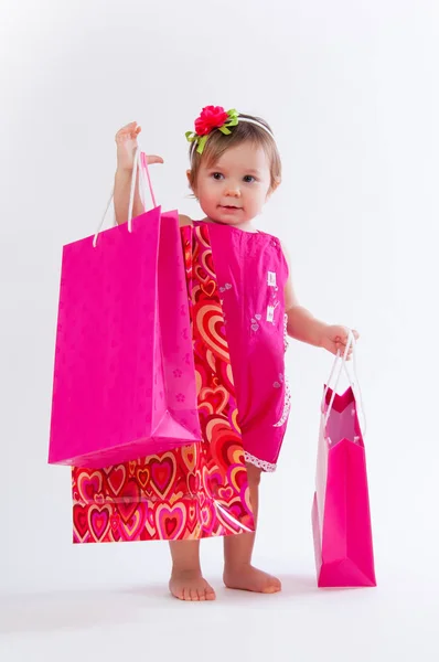 Küçük kız beyaz arka plan üzerinde izole renkli kağıt torbalar ile ayakta. — Stok fotoğraf